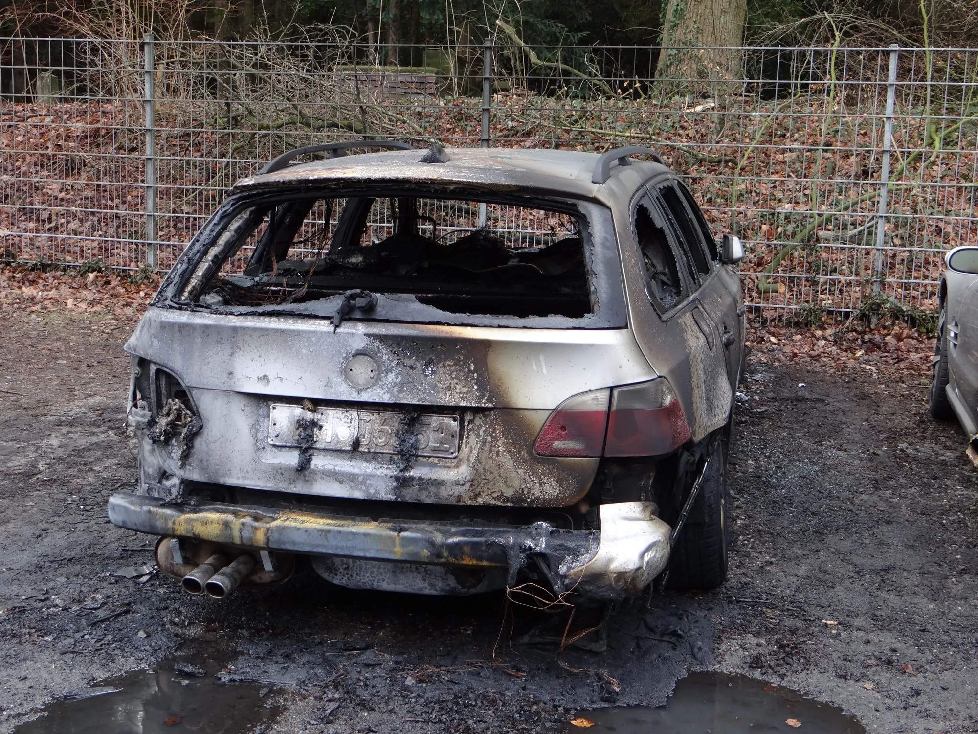 Burned-out station wagon with its rear glass gone, parked by a fence