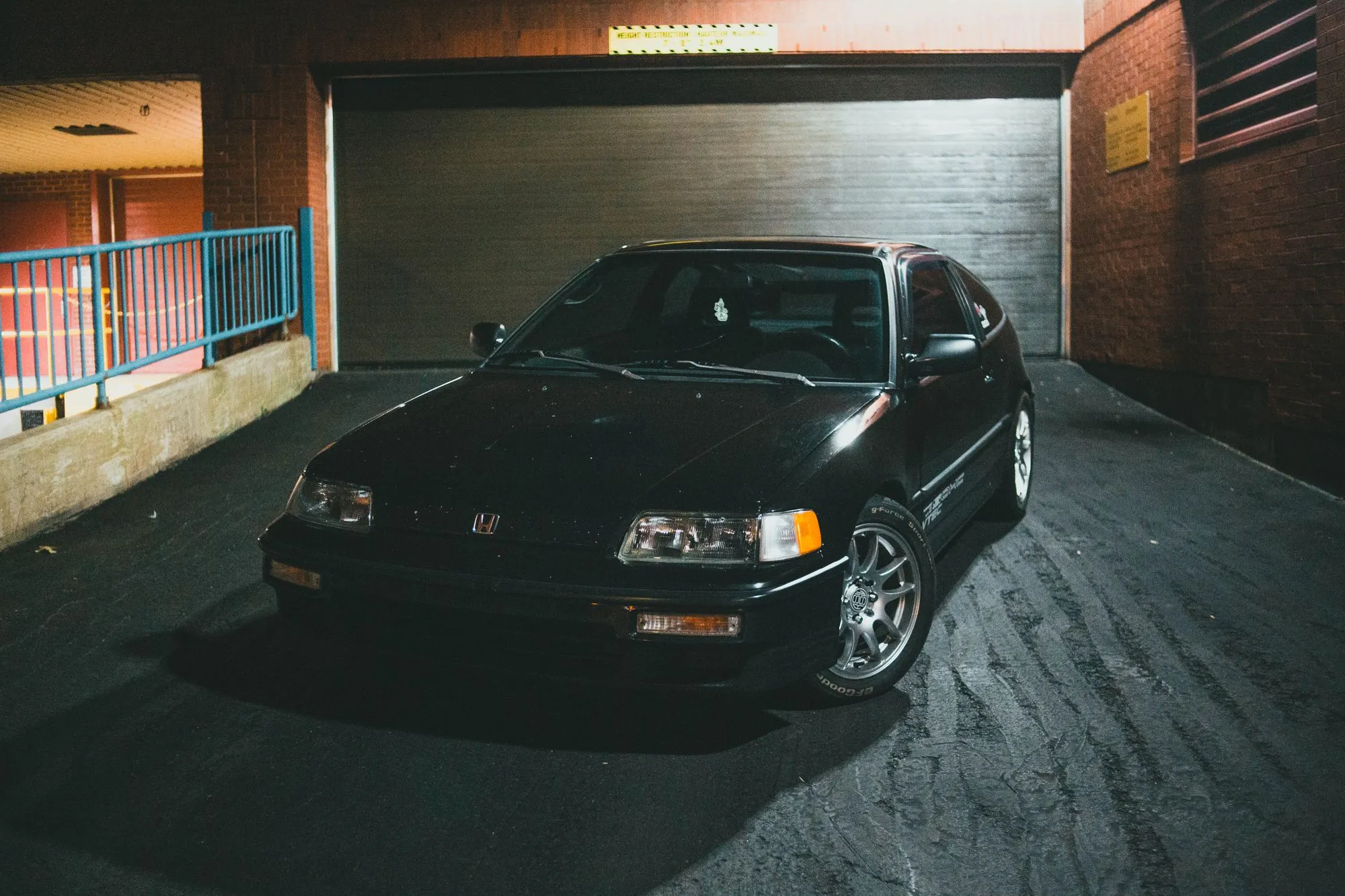 Black older sedan parked in front of an open garage at night