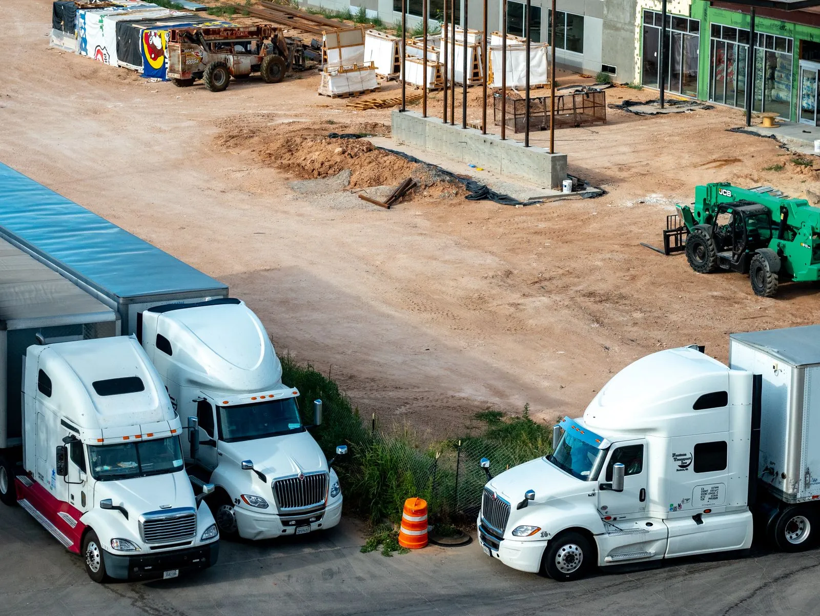 Three white semi tractors with trailers parked beside a dirt building site