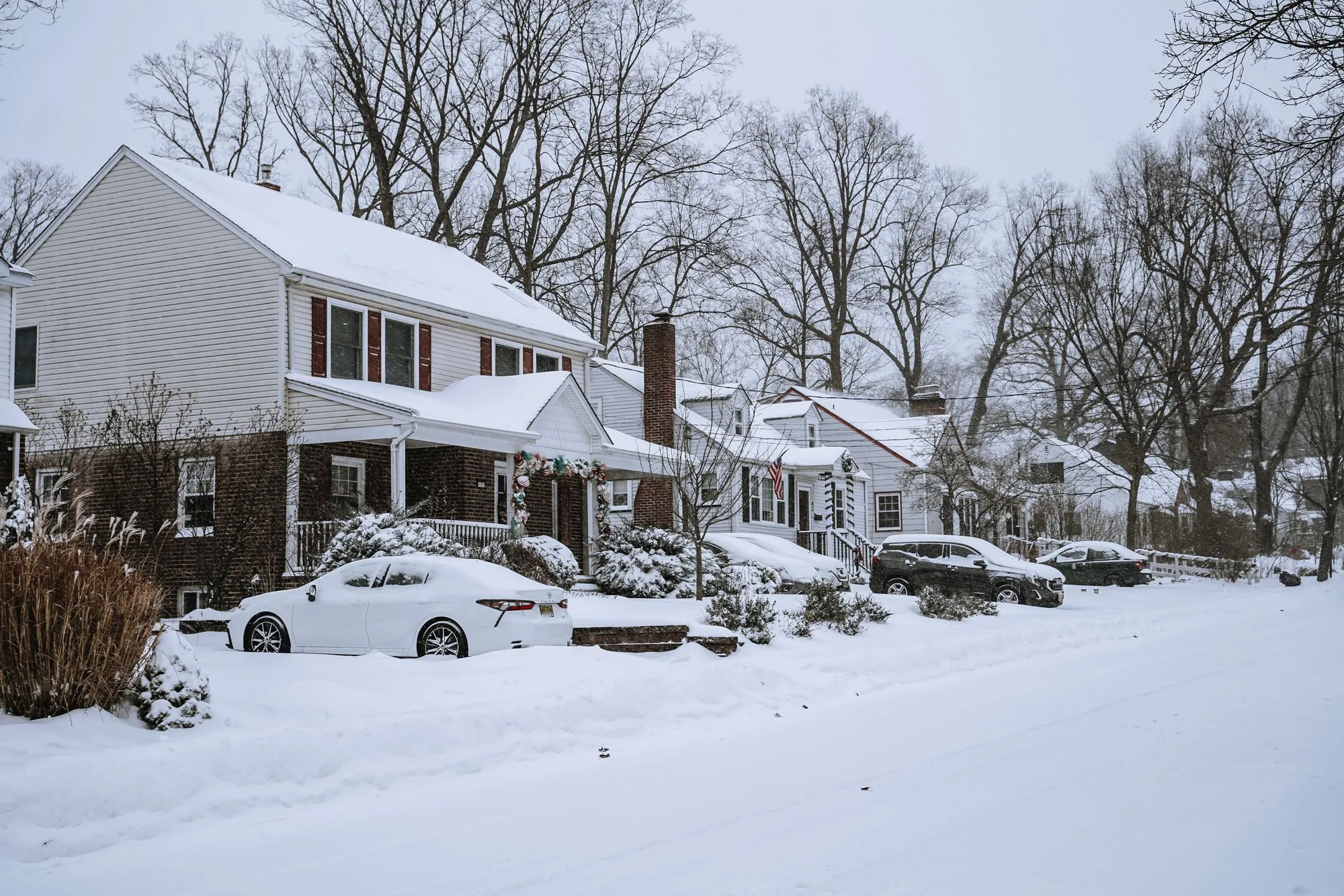 Residential street of houses after a snowfall, with parked cars covered in snow